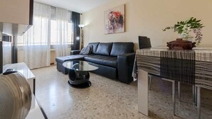 Un salón moderno con un sofá de cuero negro, una mesa de centro de vidrio y una mesa de comedor con mantel estampado.