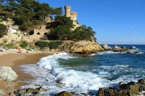 A coastal scene with a castle on a cliff, beach, and rocky shoreline.