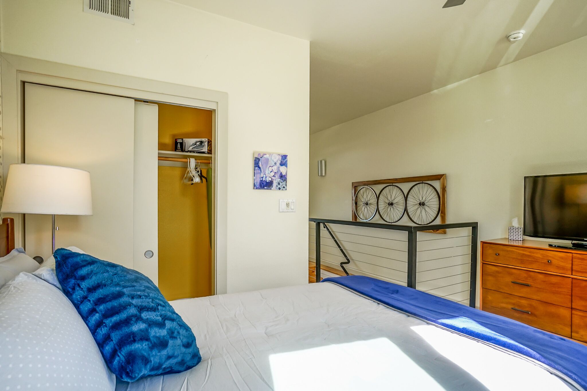 A bedroom with a bed, a dresser, a television, and a bicycle mounted on the wall.