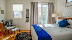 A bedroom with a bed, a chair, a desk, a mirror, and a window.