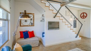 A modern living room with a staircase, a sofa, a lamp, and a TV mounted on the wall.