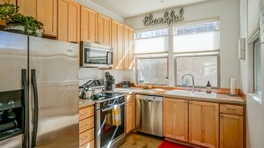 A modern kitchen with wooden cabinets, stainless steel appliances, a red rug, and a window with blinds.