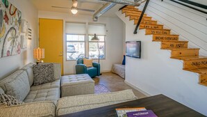 A modern living room with a sofa, ottoman, and a coffee table. There is a wooden staircase with motivational signs and a TV mounted on the wall.
