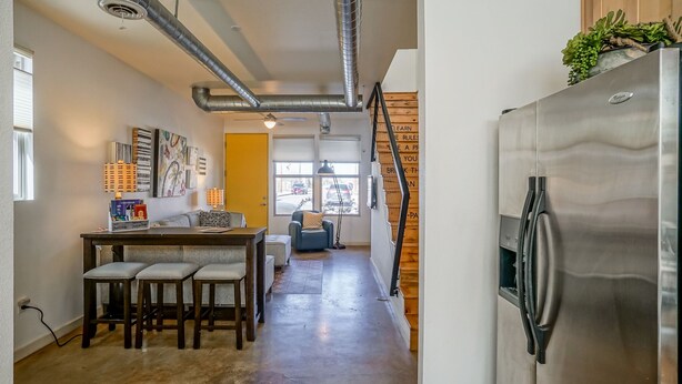 A modern kitchen with a stainless steel refrigerator, a dining area with a table and chairs, and a staircase leading to another level.