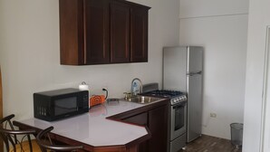 A compact kitchen with a microwave, stove, and refrigerator. There is a wooden table with chairs and a white countertop.