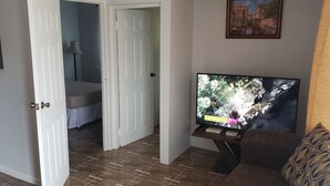 A living room with a television, a sofa, and a bed in the background.