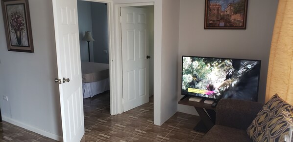 A living room with a television, a sofa, and a bed in the background.