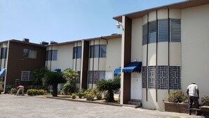 A row of modern buildings with large windows and balconies, surrounded by well-maintained landscaping and a clear sky.