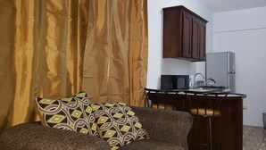 A living room with a sofa, a patterned pillow, a kitchen area with a microwave, and a cabinet.