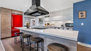 Une cuisine moderne avec un îlot central, des tabourets de bar et un réfrigérateur rouge.
