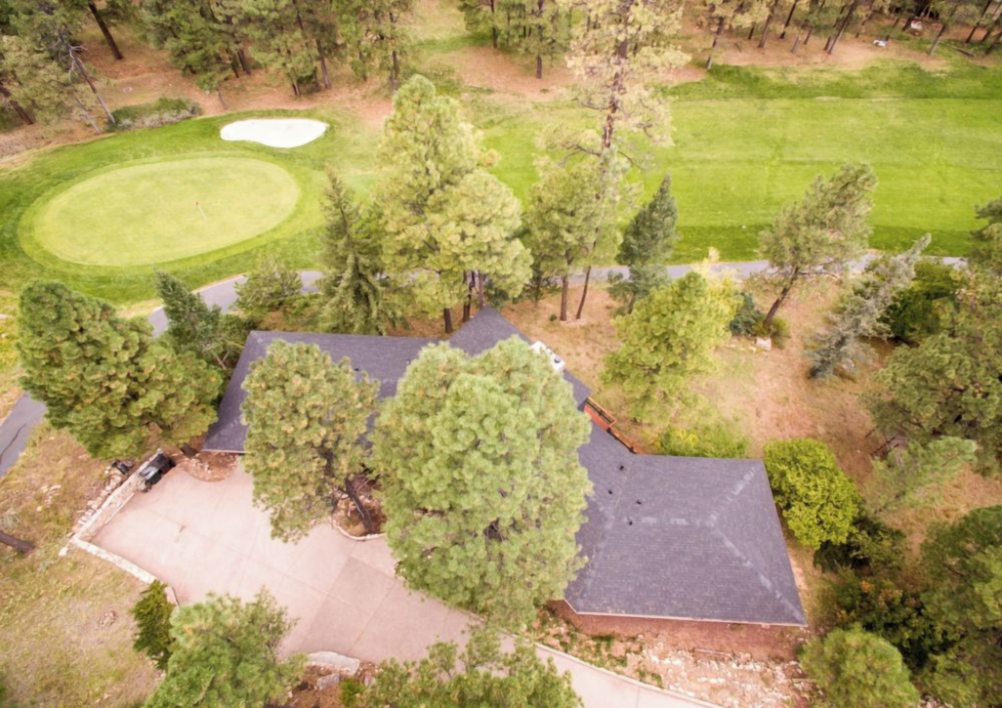An aerial view of a property with a golf course, a large tree, and a building with a sloped roof.