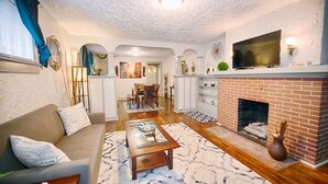 A living room with a sofa, coffee table, fireplace, TV, and a dining area with chairs and a table. - Quiet Street 10 minutes from Downtown Indy! #1 (Indianapolis)