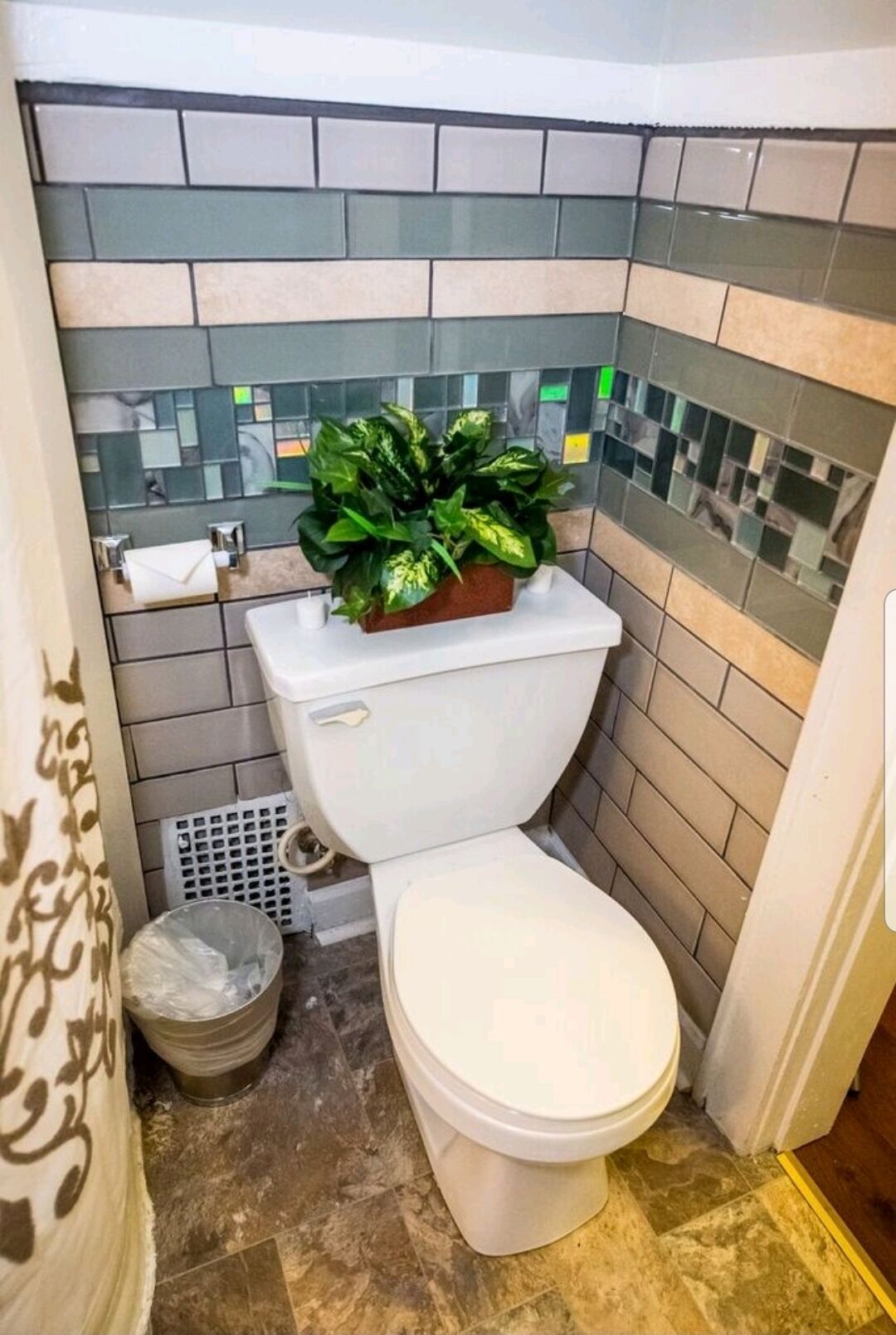 A bathroom with a toilet, a trash bin, and a potted plant on the toilet tank.