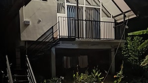 Una casa de dos pisos con balcón, escaleras y entrada protegida por una reja.