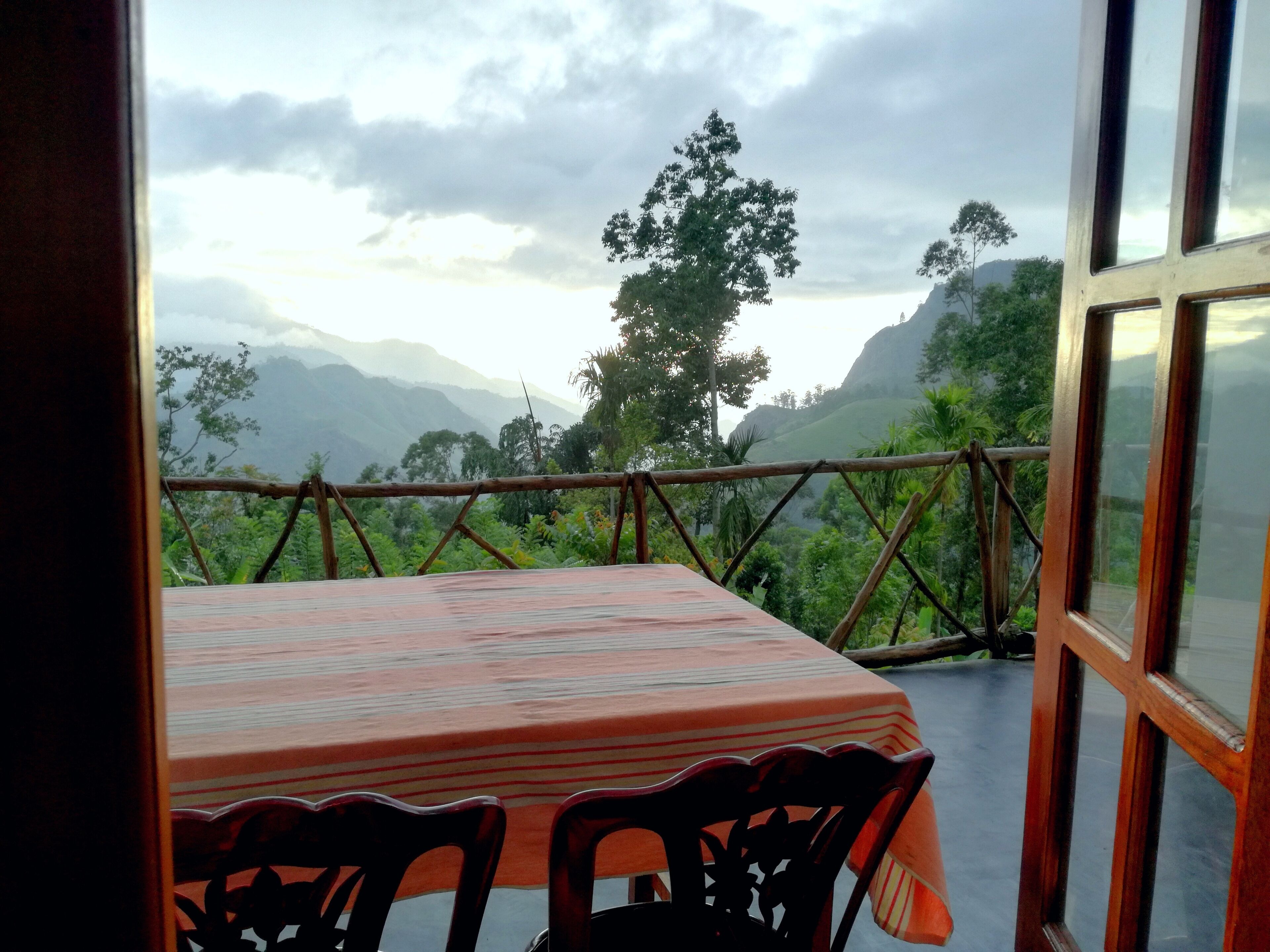 A table with chairs on a balcony overlooking a mountainous landscape.