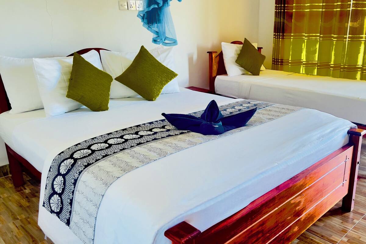 Una cama doble con sábanas blancas, una toalla decorativa azul, dos almohadas y un corredor de cama estampado.