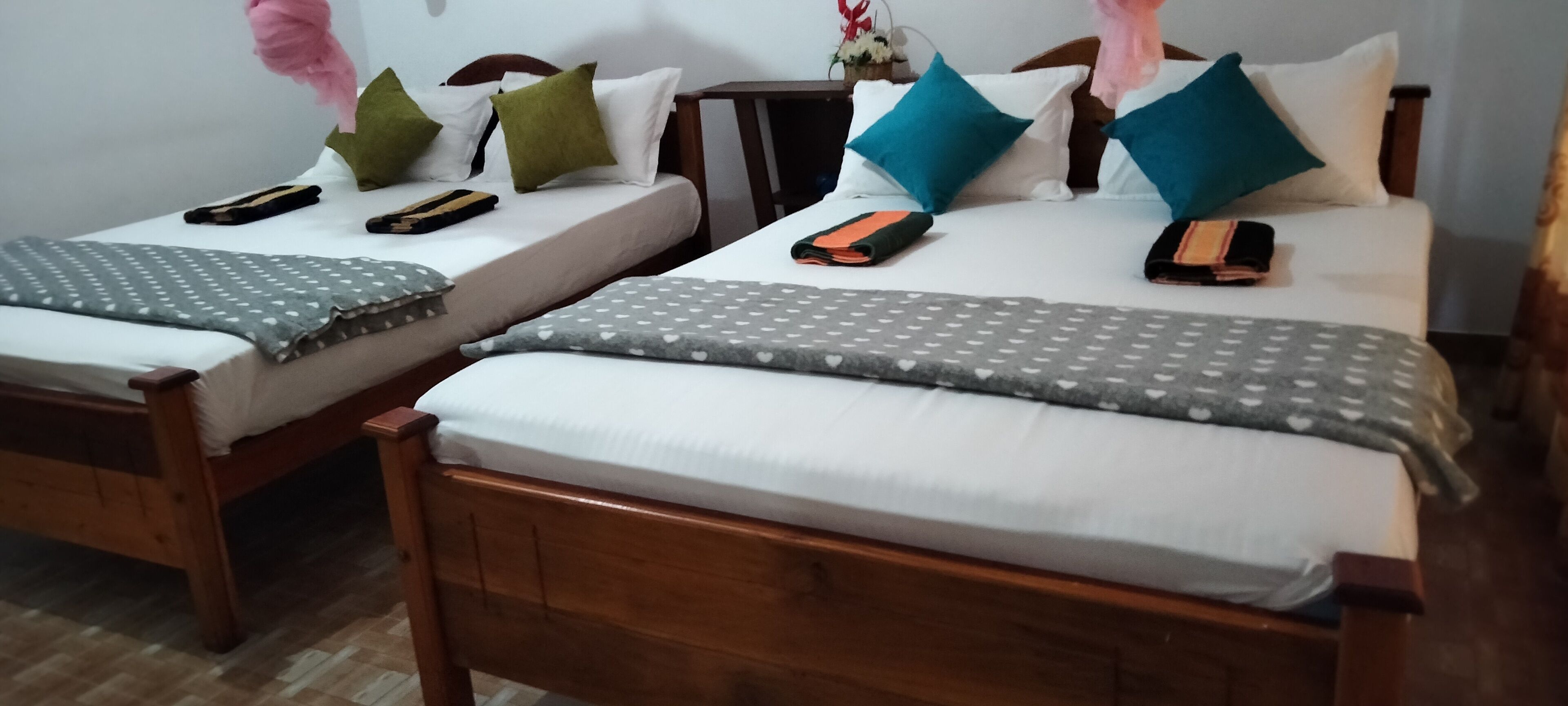 Dos camas de madera con sábanas blancas, cada una con una manta gris de lunares y varias almohadas.