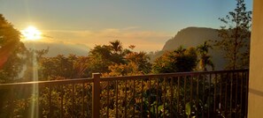 Balcón con vista a un paisaje montañoso y vegetación exuberante al amanecer o al atardecer.