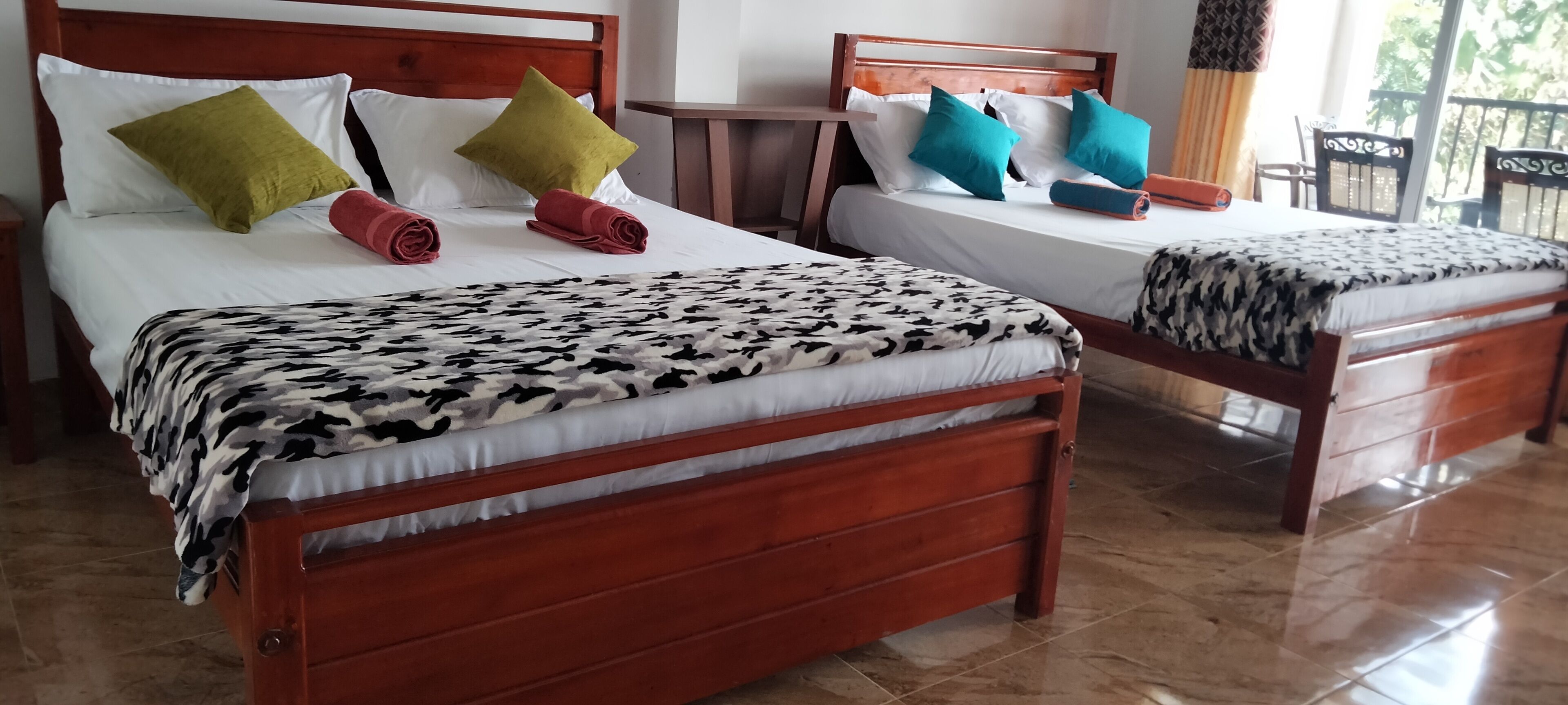 Two wooden beds with white linens and patterned blankets, each with pillows in different colors.