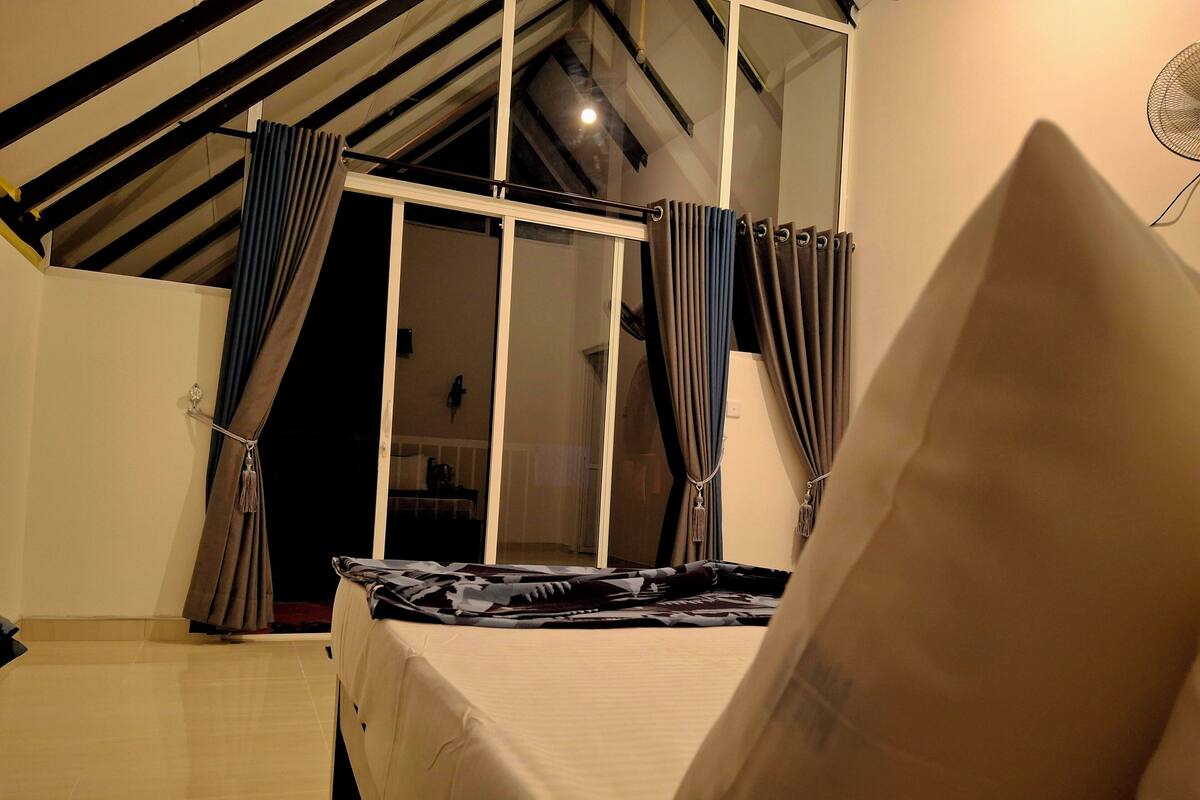 Un dormitorio con cama, ventana con cortinas y tragaluz.