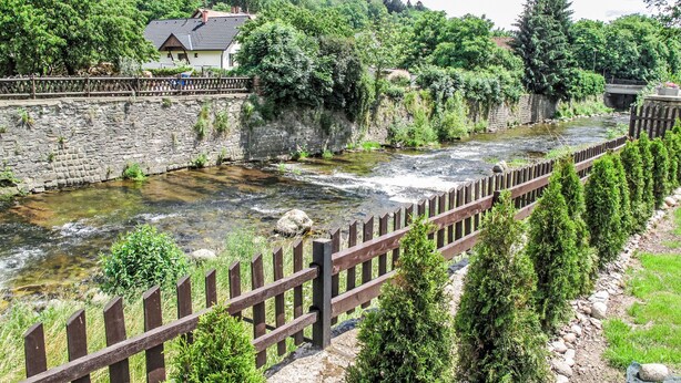 A stone bridge over a river, surrounded by greenery and a wooden fence.