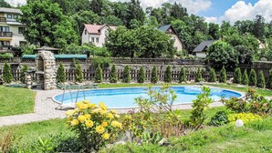 A swimming pool surrounded by a stone wall, with a stone structure and a wooden fence in the background.