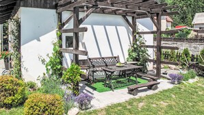 A wooden pergola with a table and benches in a garden area.