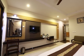 A hotel room with a bed, a television, a mirror, a small table with a coffee maker, and a chair. - Hotel Mayas (Tiruchirappalli)