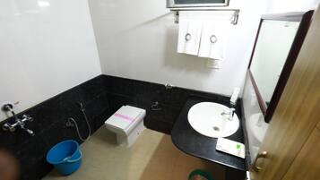 A small bathroom with a white sink, black countertop, and a mirror. There is a blue bucket on the floor and a green trash bin.