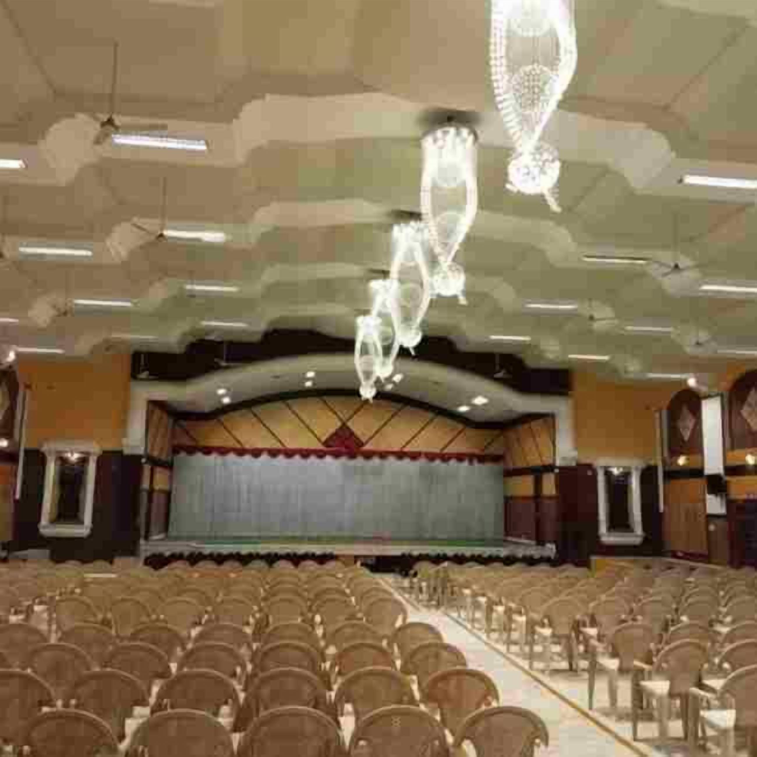 Une grande salle avec des rangées de chaises, une scène et un plafond orné de lustres.