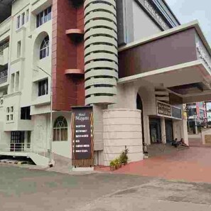 A multi-story building with a prominent cylindrical structure, a signboard with text, and a staircase leading to an entrance. - Hotel Mayas (Tiruchirappalli)