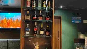 A bar area with shelves of liquor bottles, a television screen, and a wooden cabinet. - Hotel Mayas (Tiruchirappalli)
