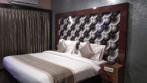 A modern bedroom with a large bed, a wooden headboard, and a nightstand. - Hotel Mayas (Tiruchirappalli)