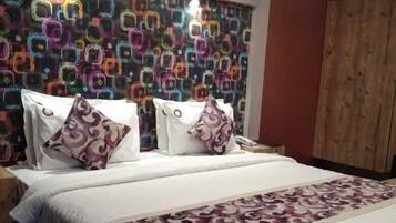 A hotel room with a patterned headboard, a large bed with a patterned bedspread, and a wooden wardrobe.