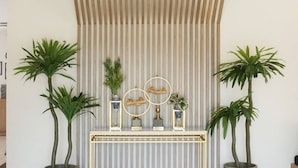 A reception area with a modern design, featuring a slatted wooden ceiling, a central console with decorative items, and two potted plants. - Hotel Matana (Chiang Mai)