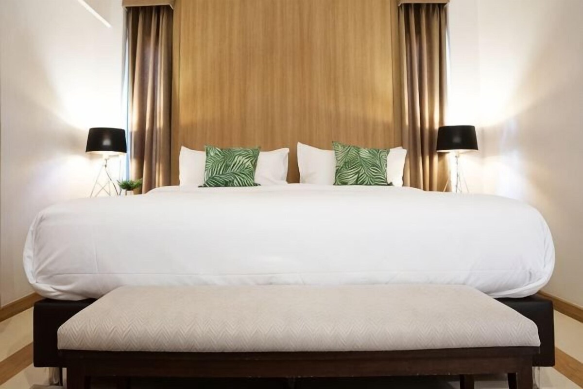 A large bed with white bedding, two bedside lamps, and a wooden headboard.