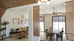 A modern interior with a dining area, a seating area with a sofa, and a large window providing natural light. - Hotel Matana (Chiang Mai)
