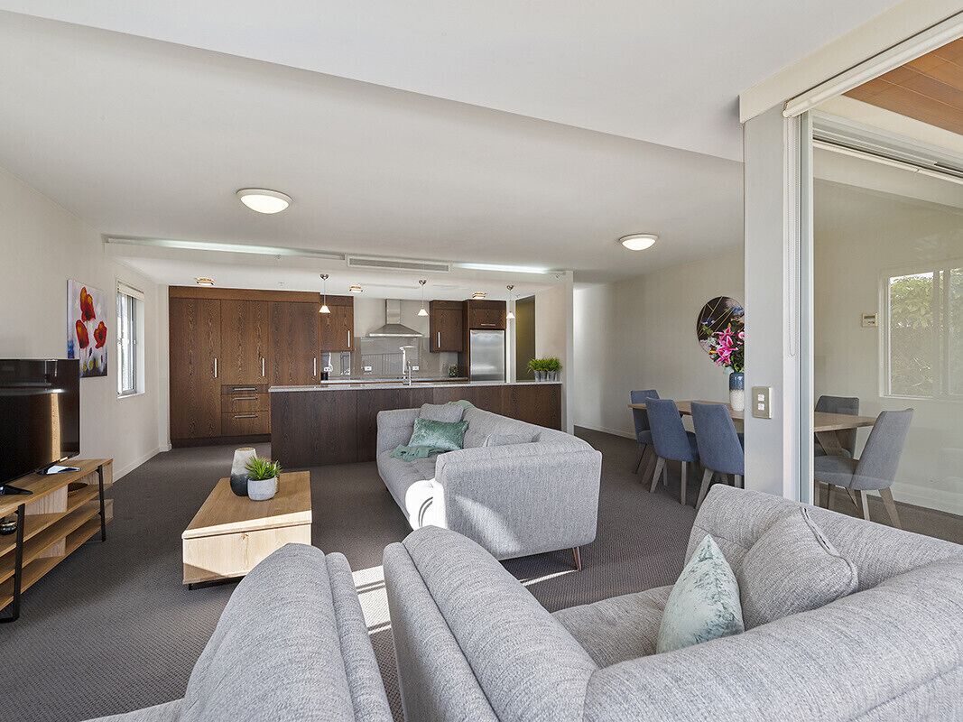 A modern living room with grey sofas, a coffee table, and a kitchen in the background.