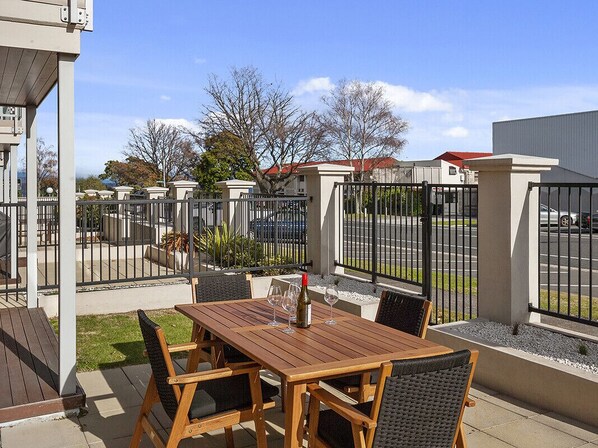 An outdoor patio with a wooden table and chairs, a bottle of wine, and a glass. - Roberts Retreat - Taupo Holiday Home (Taupo Central)