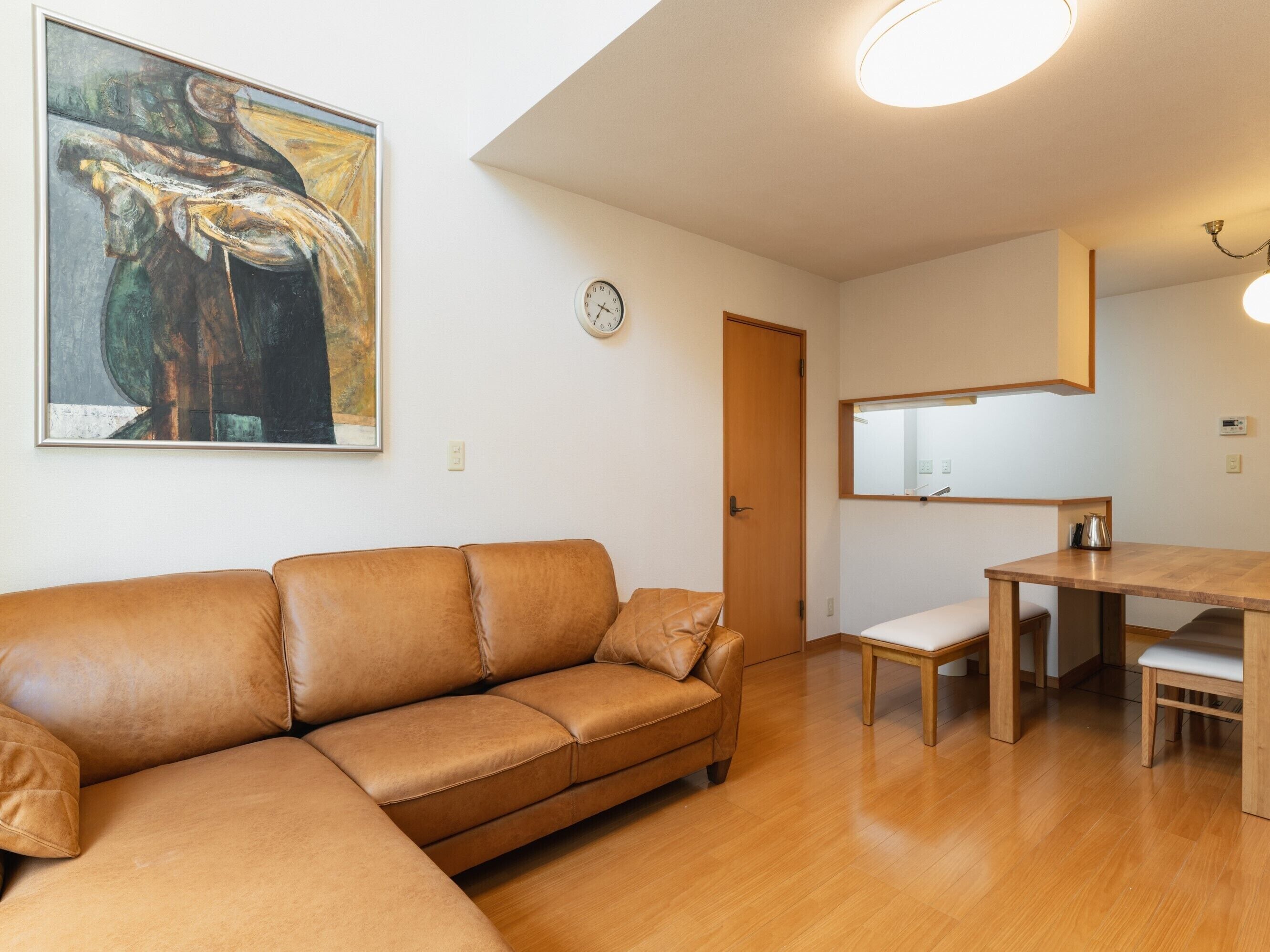 A living room with a brown leather sofa, a wooden dining table, and a painting on the wall.