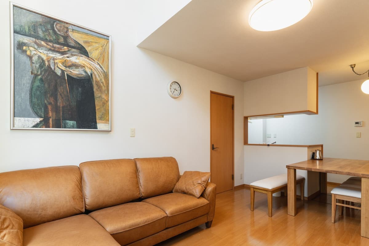 Una sala de estar con un sofá de cuero marrón, una mesa de comedor de madera y un cuadro en la pared.