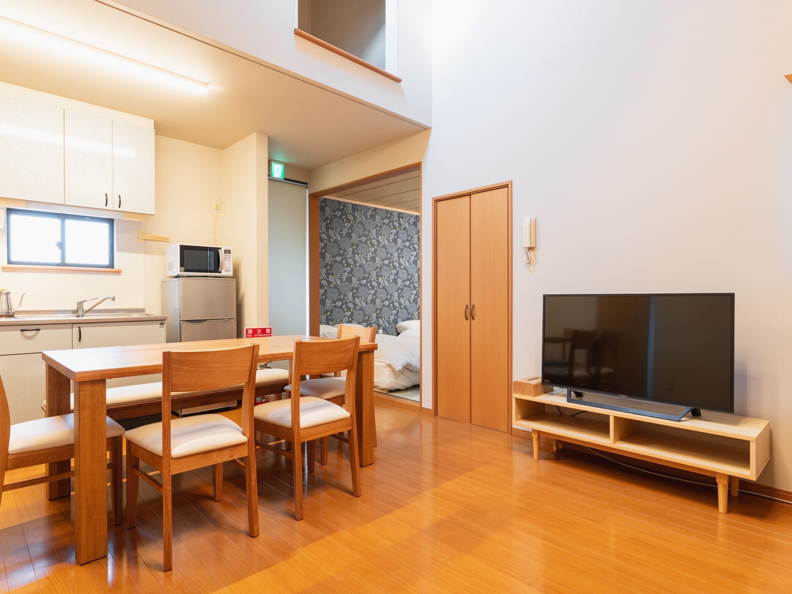 A modern kitchen with a microwave, a dining table with chairs, a TV on a stand, and a wardrobe.