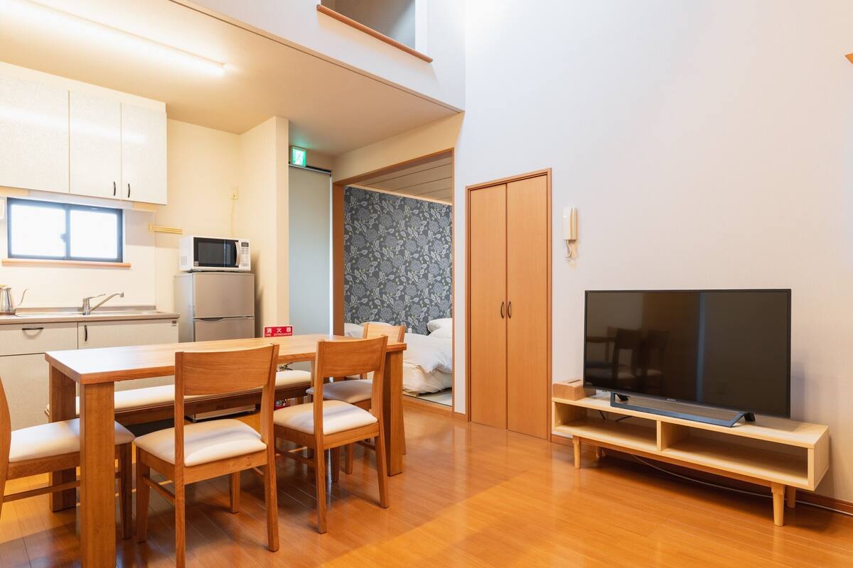 Una cocina moderna con microondas, una mesa de comedor con sillas, un televisor sobre un mueble bajo y un armario.