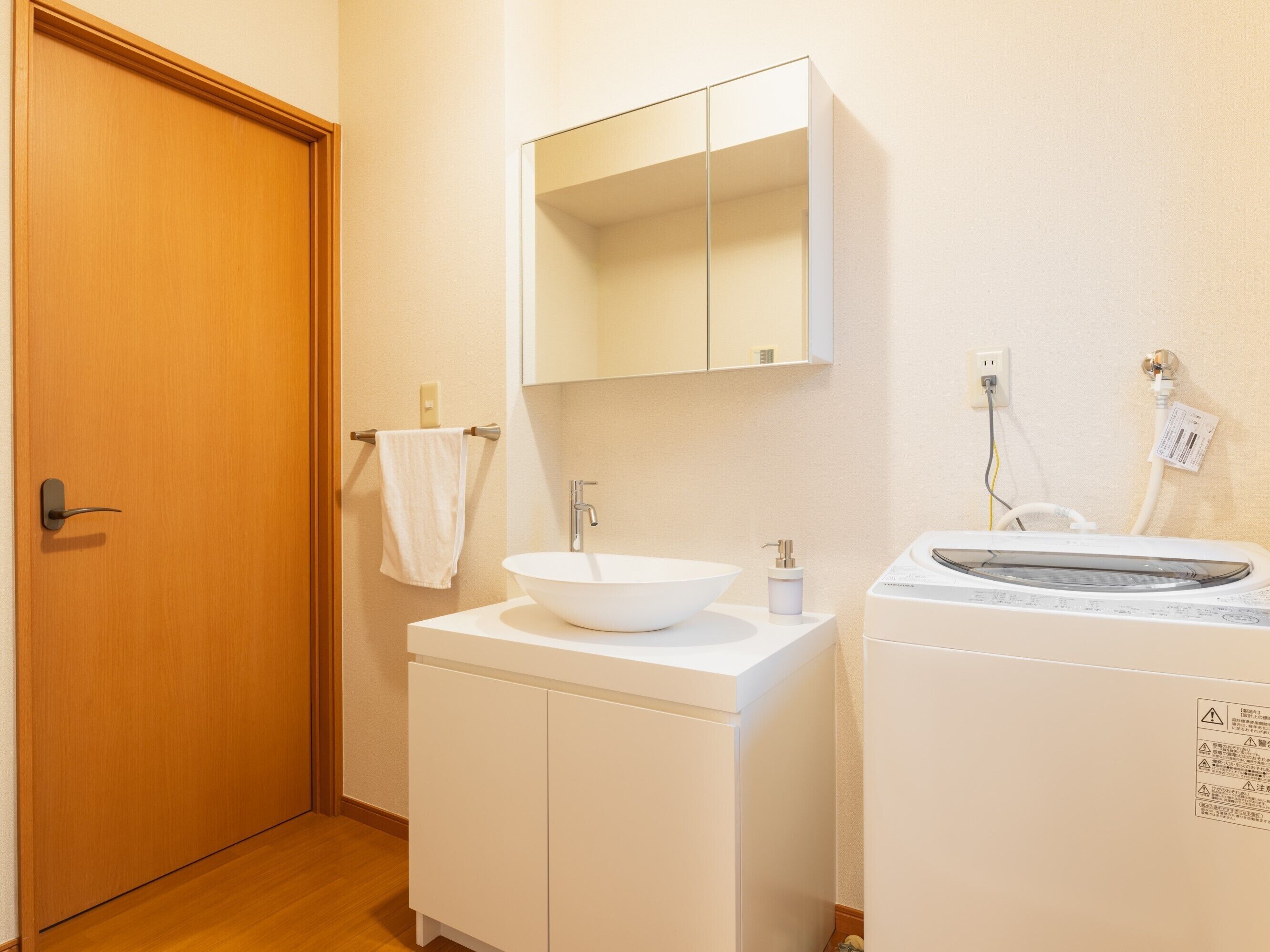 A bathroom with a wooden door, a white sink with a mirror above it, and a washing machine.