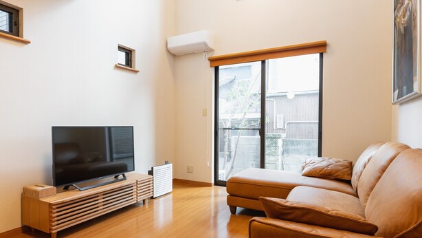 Una sala de estar moderna con televisor de pantalla plana, mueble de entretenimiento de madera, sofá de cuero y puerta corrediza de vidrio que da a un balcón.