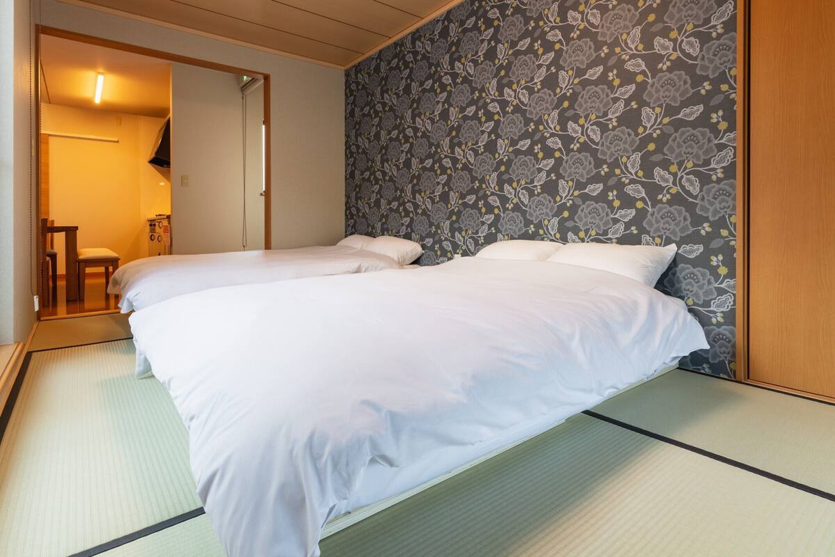 Una habitación con dos camas, una puerta de madera y un papel tapiz estampado.