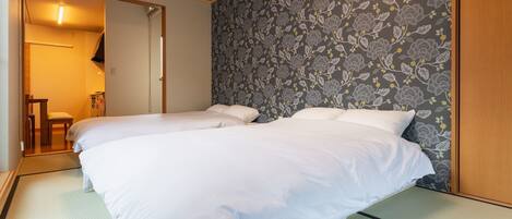 Une chambre avec deux lits, une porte en bois et un papier peint à motifs.