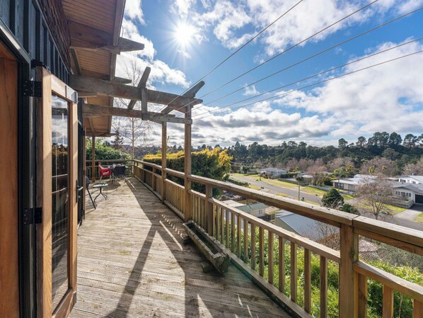 A wooden balcony with a view of a residential area, a pergola, and a table with chairs.