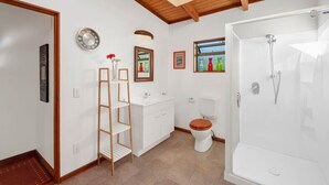 A bathroom with a wooden ceiling, a white sink, a toilet, a shower, and a mirror. - Treetop Hideaway - Taupo Holiday Home (Taupo Central)