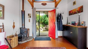 A cozy interior with a wooden ceiling, a red door, a stone wall, and a rustic fireplace. - Treetop Hideaway - Taupo Holiday Home (Taupo Central)